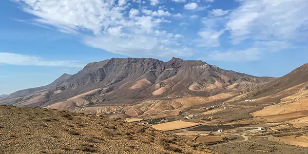 volcanic landscape in Fuerteventura, with desert and fields in the foreground and a blue sky in the background