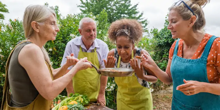 A group of friends learning to cook on holiday, stood around a table and admiring the fresh produce