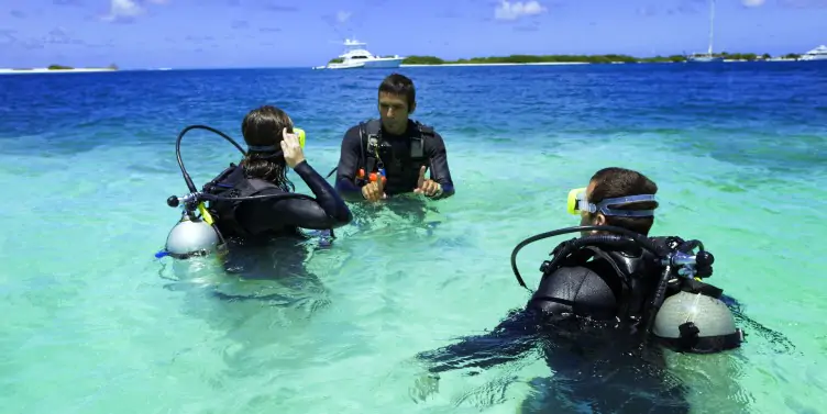 Three people in the sea, all wearing scuba diving gear on a learn to dive holiday 