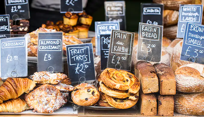 a selection of sweet foods at a food stall with prices, including croissants and fruit tarts