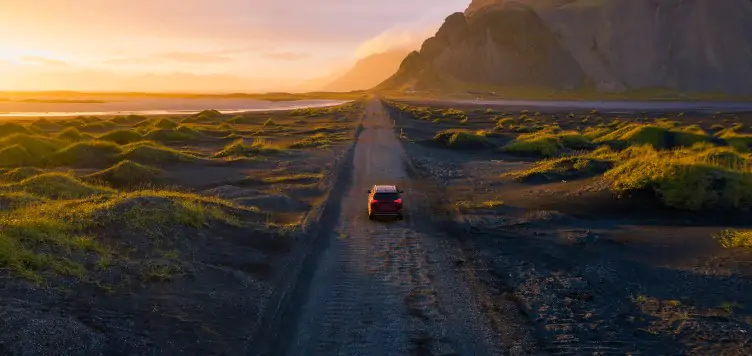 A car drives on a gravel road with the stunning Vestrahorn Mountain as the backdrop during an Icelandic sunset, highlighting the possibility of renting a car in Europe for an unforgettable journey.