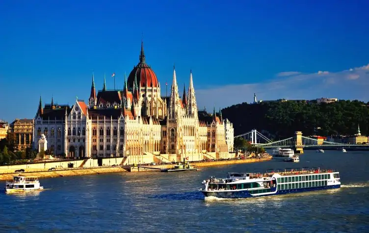 View of the hungarian parliament bulding from across the river. River cruise boat is sailing along the water.