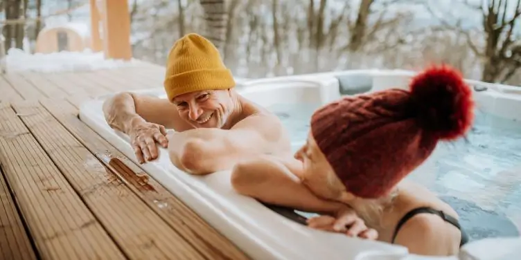 Senior couple enjoying an outdoor hot tub on a winter's day. Both are wearing bobble hats,