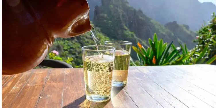 A jug of wine being poured into glasses overlooking green valleys in Tenerife