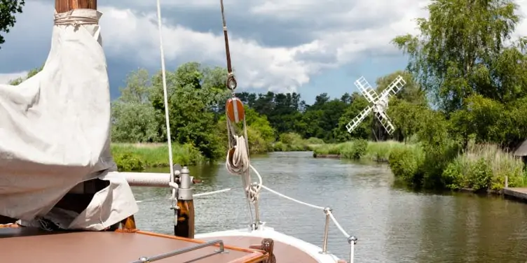 Boat sailing on the Norfolk Broads with a windmill in the background and windmill on river on Norfolk Broads
