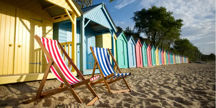 an image of two deck chairs in front of beach huts on a beach in the UK