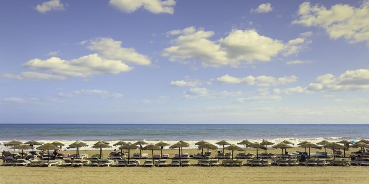 Sunbeds and parasols lining the shore of a golden sandy beach in Estepona