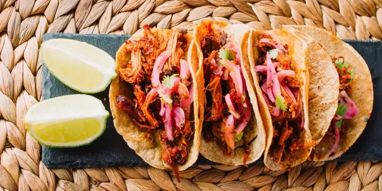 a platter of cochinita pibi tacos with lemon slices, a traditional dish from Mexico