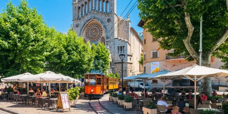 The historic tram of the Soller tramway line driving through tables of diners in a street in Soller, Mallorca