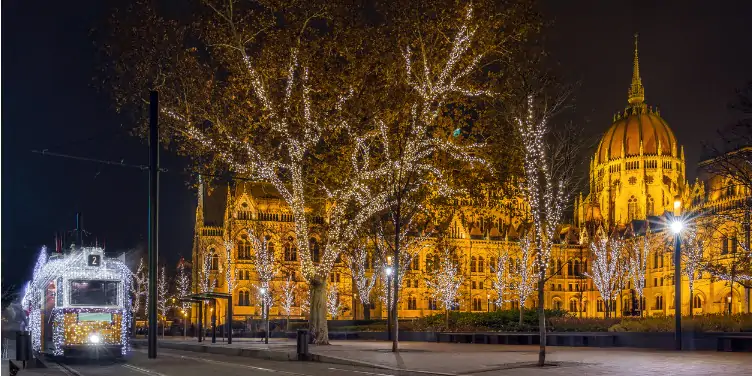 Festive tram covered in lights passing the Parliament of Hungary in Budapest