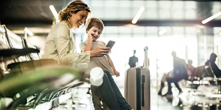 Mother and son sitting, waiting for their flight both laughing at something on their phones. 