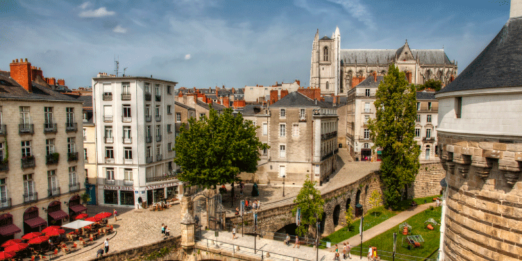 Birdseye view of the city of Nantes with St. Peter Cathedral in the distance, as tourists and locals walk across the bridge which leads into the Castle of Brittany Duke’s. 