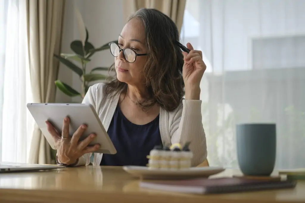 mature woman sitting in bright living room and using digital tablet, surfing internet