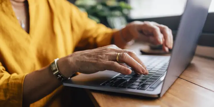 A woman holding typing on a laptop applying for her passport online.