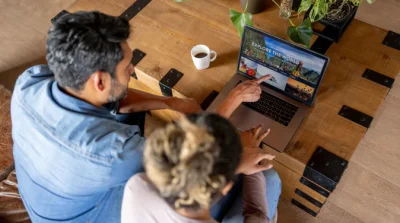A man and woman sat at a table booking a holiday on their laptop
