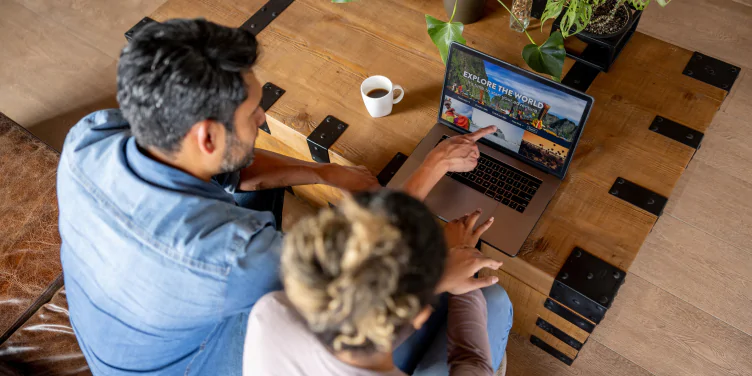 A man and woman sat at a table booking a holiday on their laptop