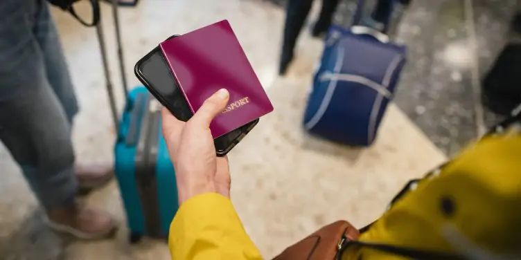 Woman in airport holding her passport and smart phone in her hand.